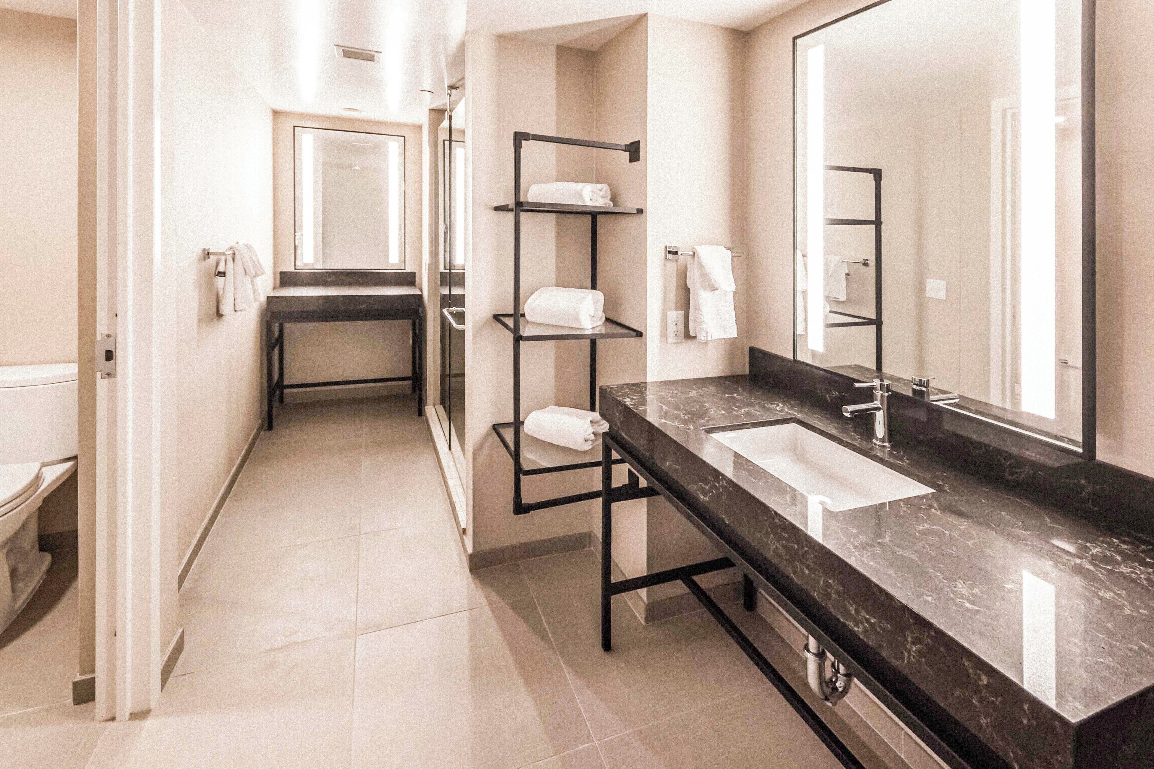 A modern bathroom with a black marble sink, a large mirror, and a towel rack.