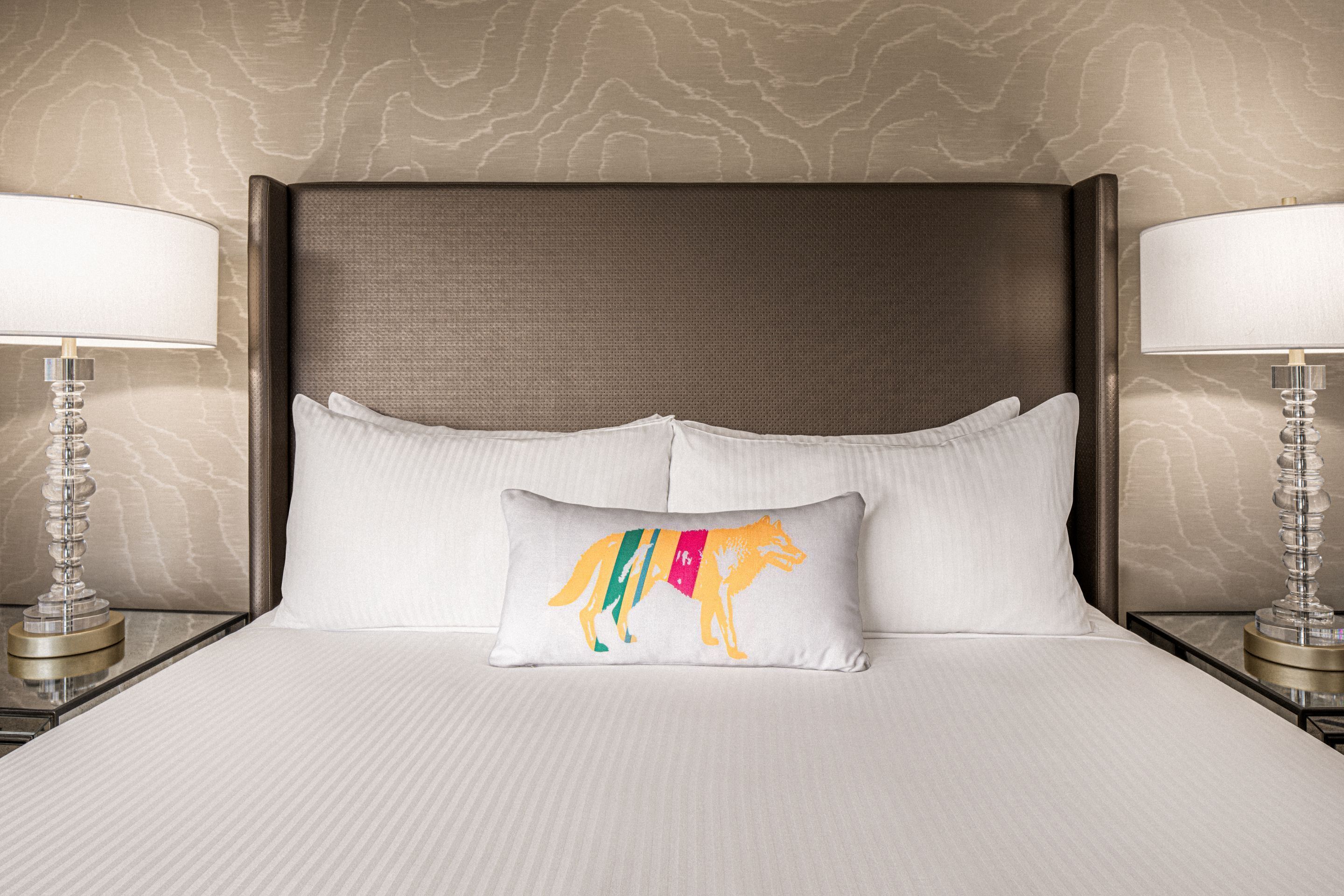 Une chambre d’hôtel avec un grand lit, deux lampes de chevet et un coussin décoratif orné d’un motif animal coloré.