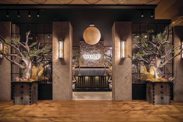 A reception area with a large wooden sign reading 'WOLF,' a stone wall, and two large trees with branches.