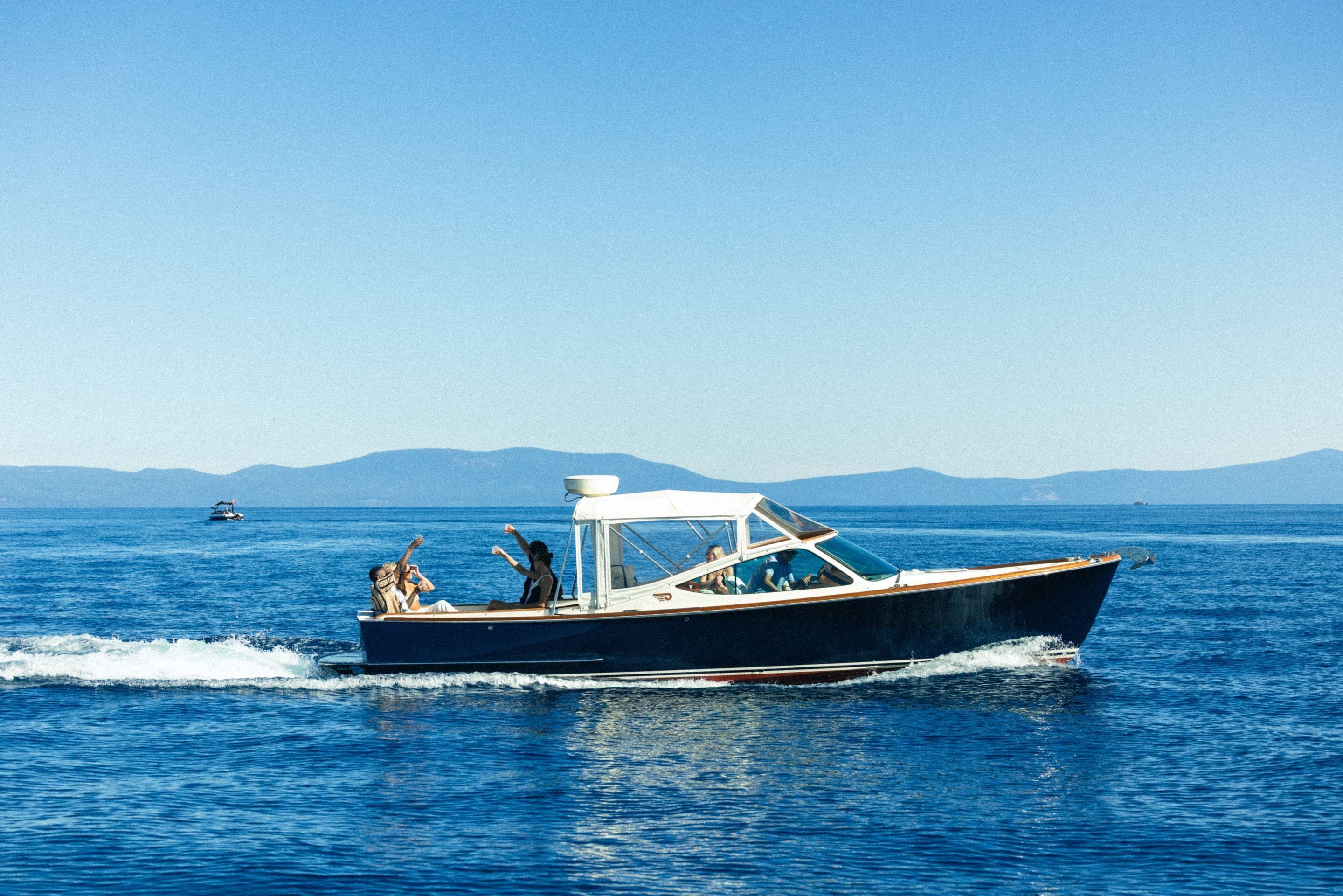 A boat with passengers, moving on a body of water with distant landforms.