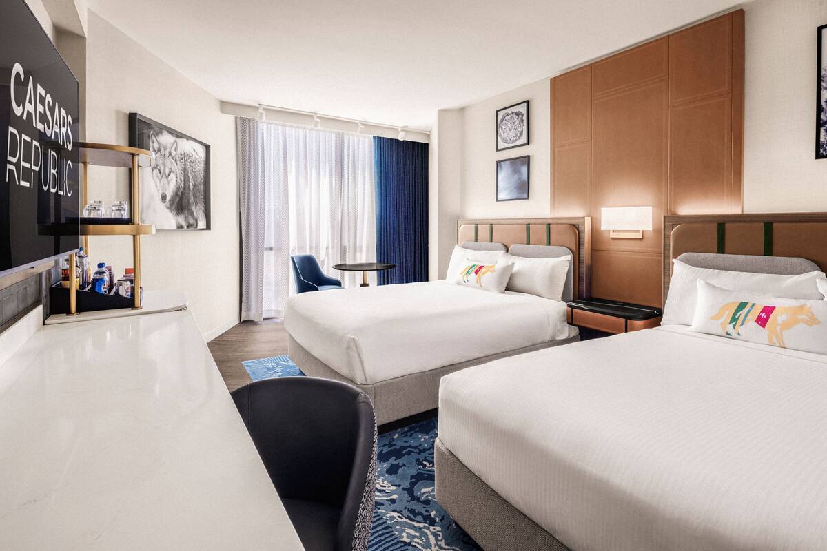 Ein Hotelzimmer mit zwei Betten, einem Schreibtisch, einem Stuhl, einem Fernseher und einem Fenster mit Vorhängen.