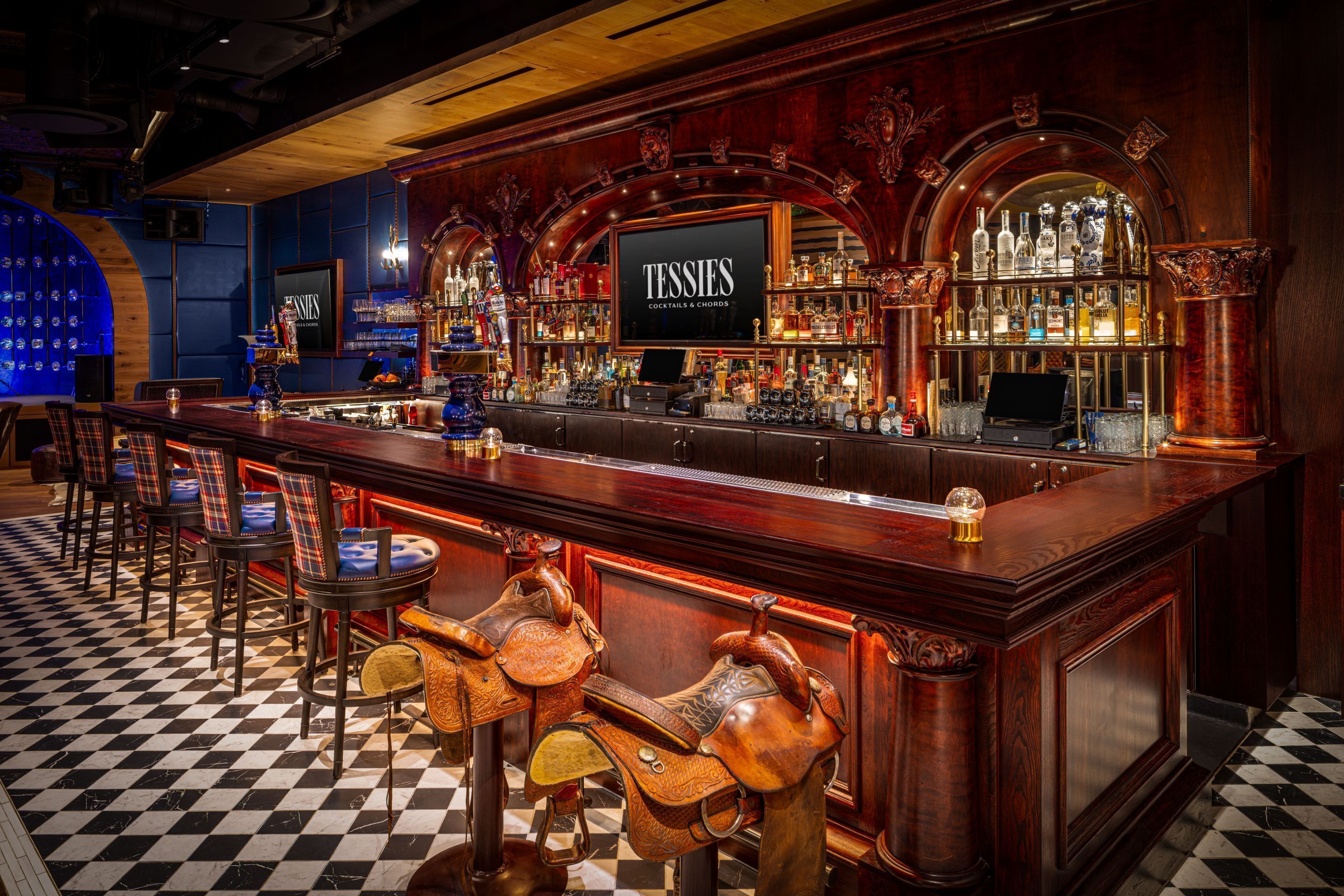 Un bar avec un sol à carreaux, des tabourets et une enseigne sur laquelle on peut lire : « TESTIES COCKTAILS & CHORDS ».