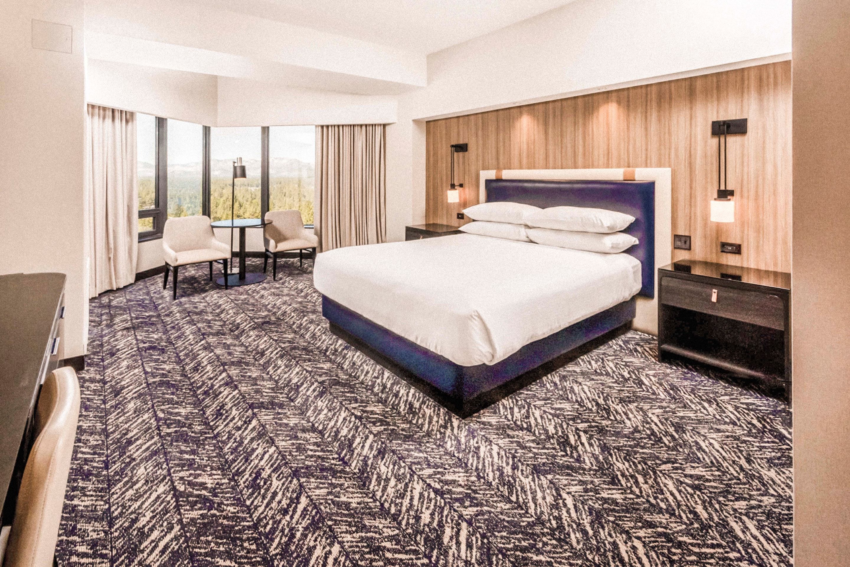 Una habitación de hotel con una cama grande, un escritorio, dos sillas y vistas al exterior.