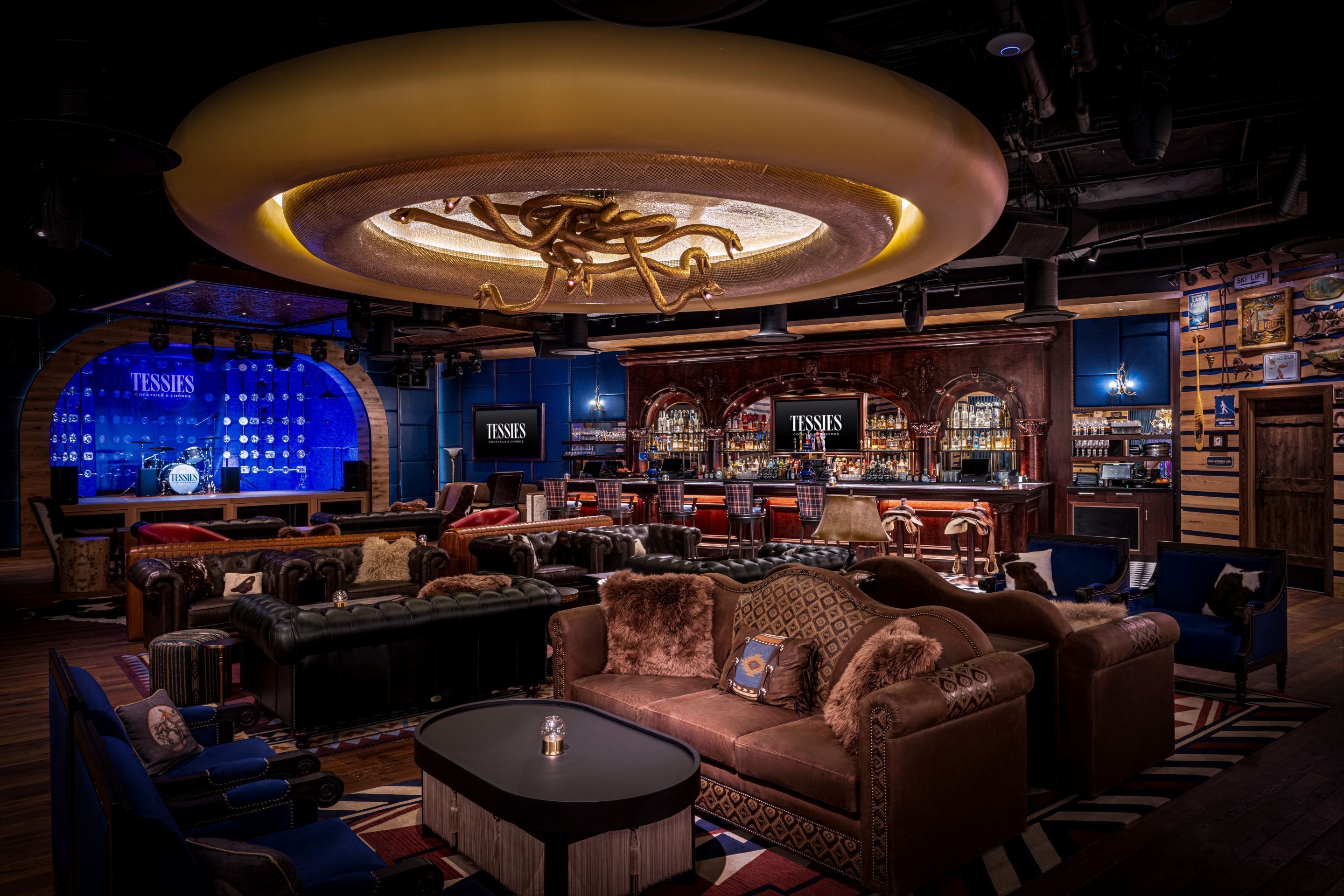 A bar area with leather seating, a DJ booth, and a large illuminated ceiling feature.
