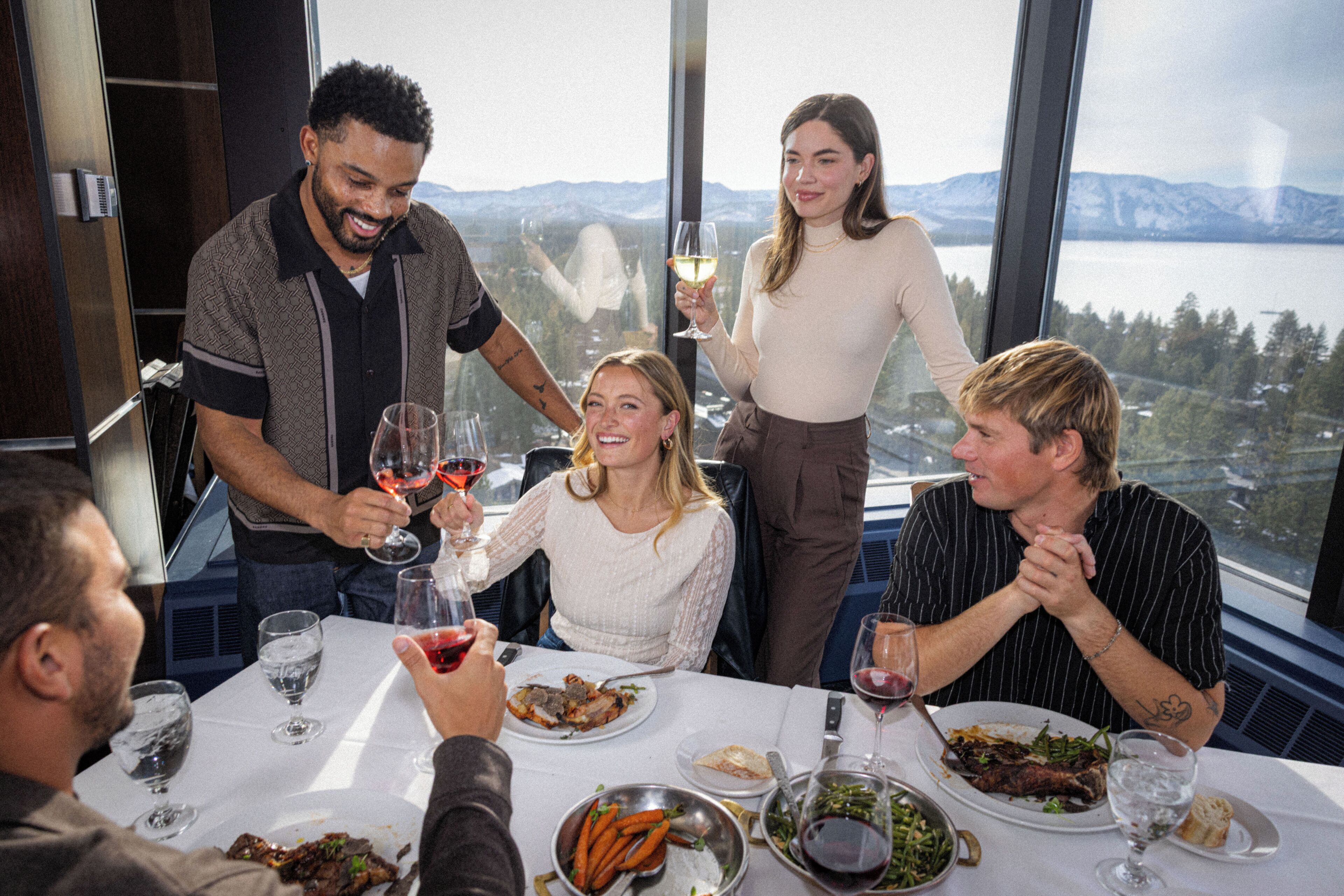 A group of people dining at a table with a view of mountains and a lake.