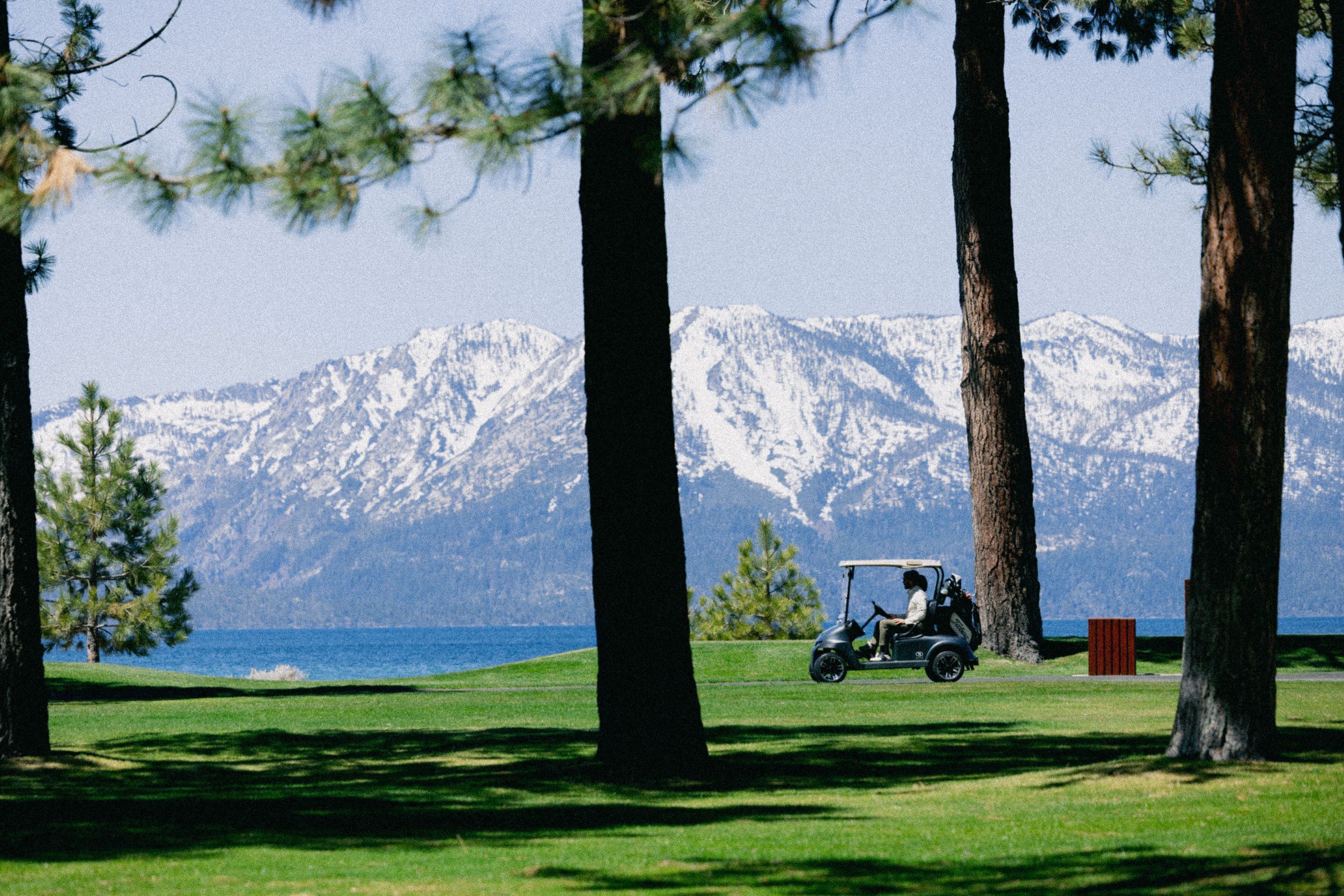 Un campo de golf con vistas a montañas nevadas y una masa de agua al fondo.