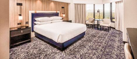 A hotel room with a large bed, a desk, two chairs, and a view of the outdoors.