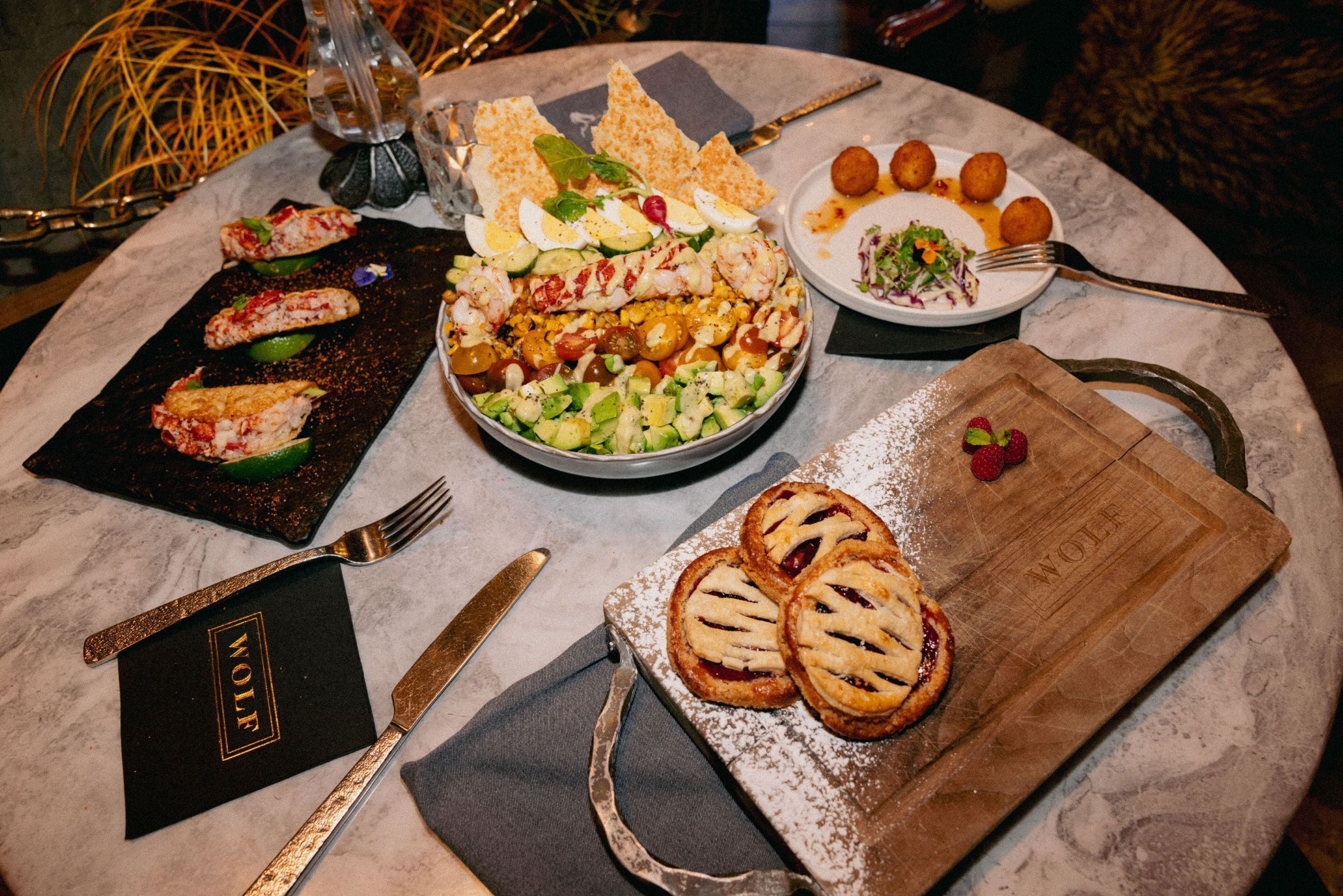 A table set with various dishes including seafood, salad, and pastries, with a menu and cutlery.
