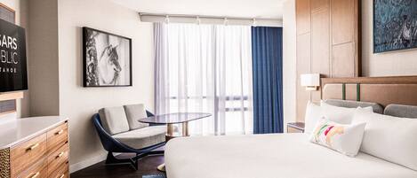 Une chambre d’hôtel avec un grand lit, un bureau, une chaise, une télévision et une fenêtre avec des rideaux.