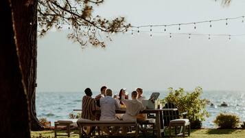 A group of people seated at a wooden table outdoors with a view of the ocean.