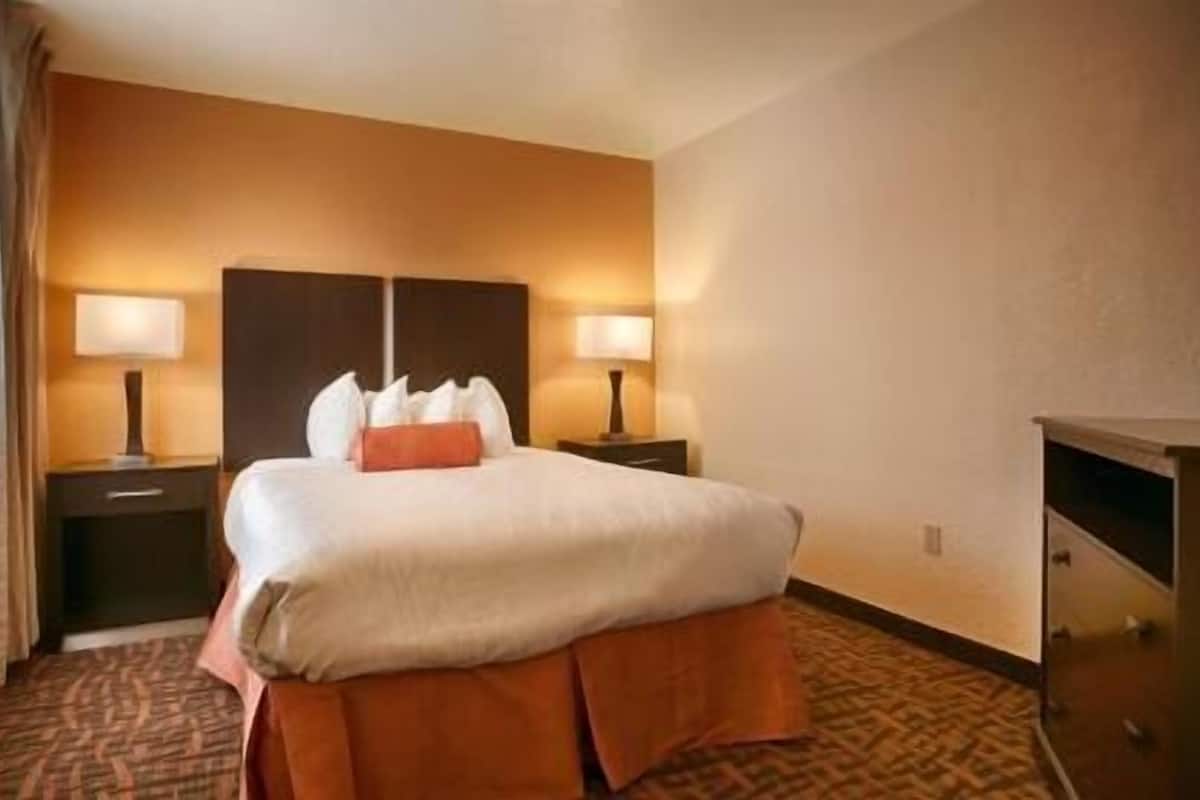 A hotel room with a bed, two bedside tables with lamps, a dresser, and a carpeted floor.