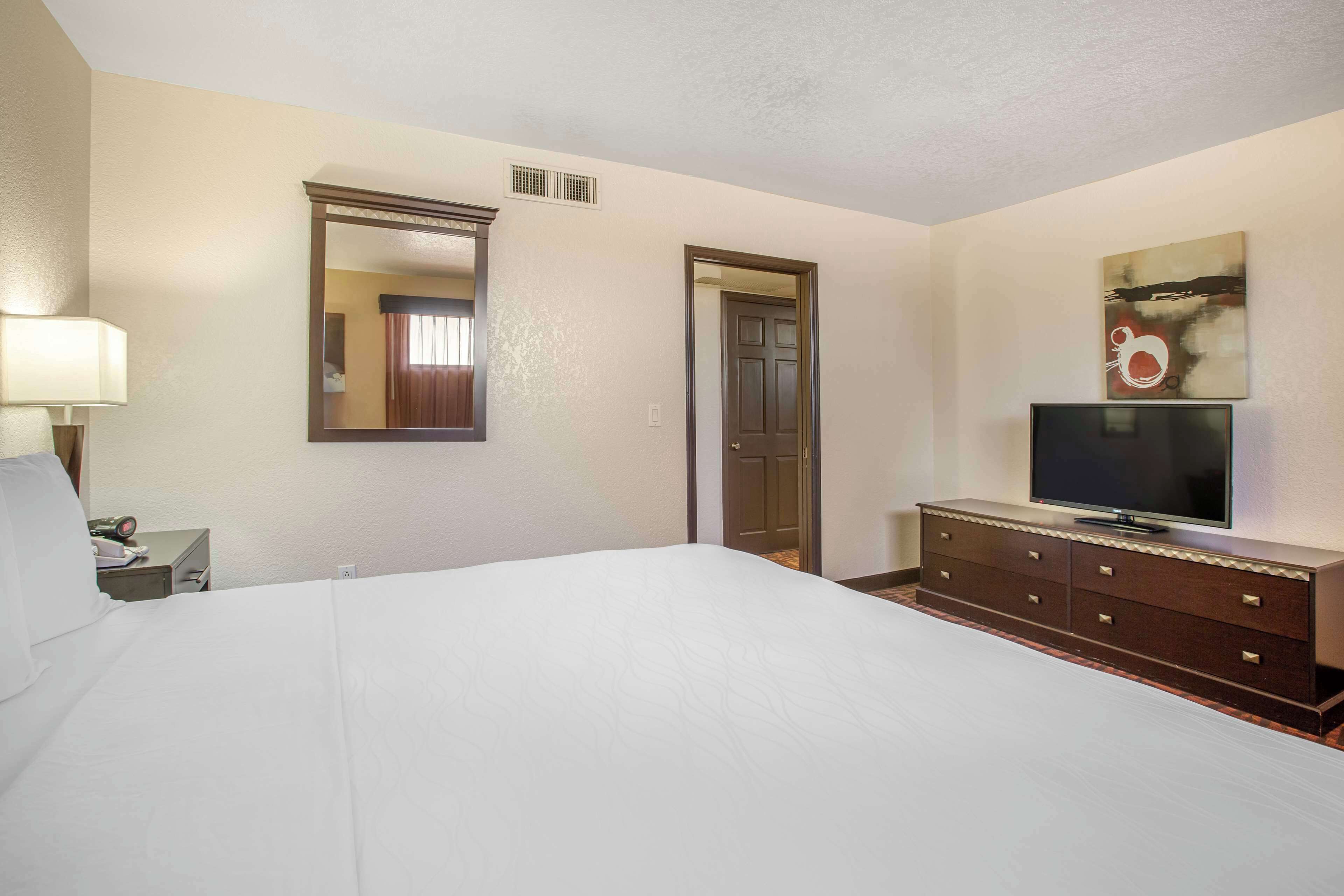 Una habitación de hotel con una cama grande, un tocador con televisor de pantalla plana, un espejo y una puerta.