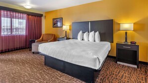 Ein Hotelzimmer mit einem großen Bett, zwei Nachttischen, einem Sessel, einem Schreibtisch und einem Fenster mit Vorhängen.