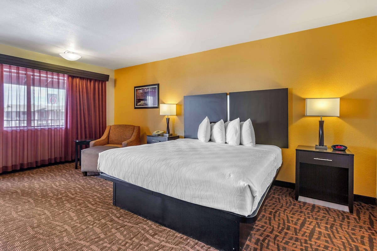 A hotel room with a large bed, two bedside tables, a chair, a desk, and a window with curtains.
