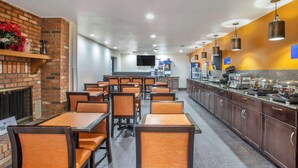 Ein Restaurant mit Ziegelwänden, Holztischen und -stühlen. Es gibt eine Theke mit Lebensmitteln und einen an der Wand befestigten Fernseher.