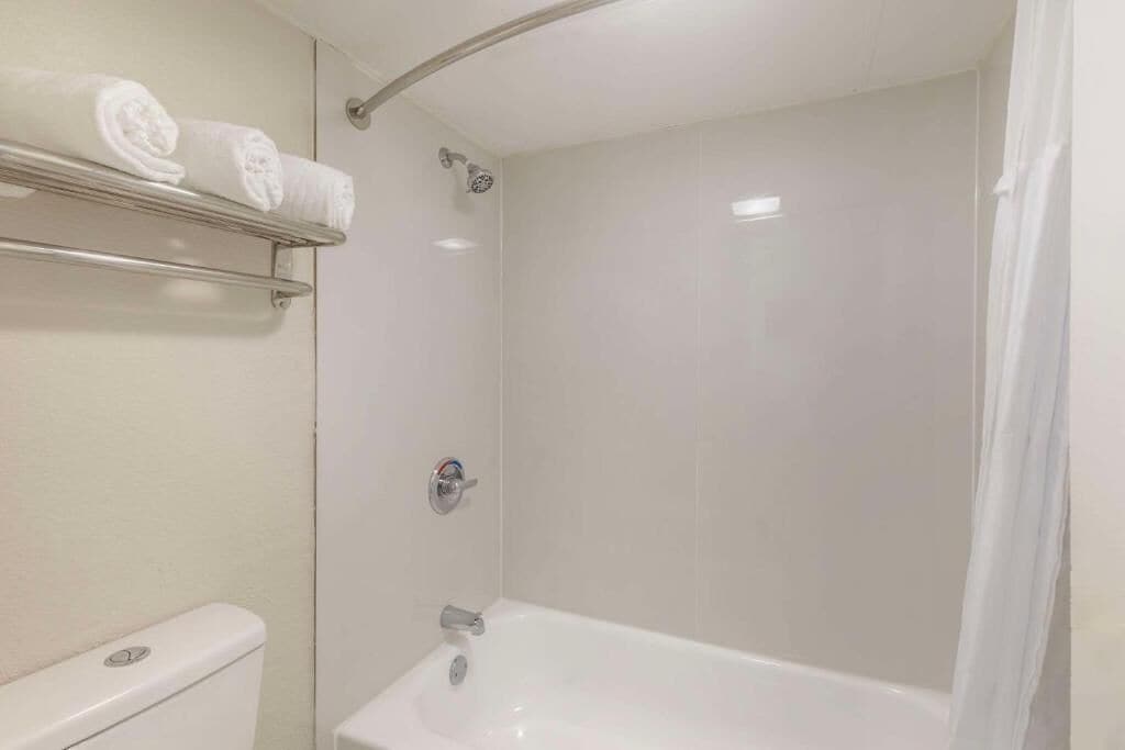 A bathroom with a white bathtub, a shower, and a toilet. There are towels on a shelf above the toilet.