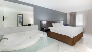 Een moderne hotelkamer met een groot bed, een aparte badkamer met bad, een grote spiegel en een nachtkastje met lamp.