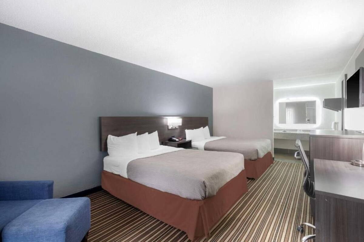 A hotel room with two beds, a desk, a chair, and a large mirror.