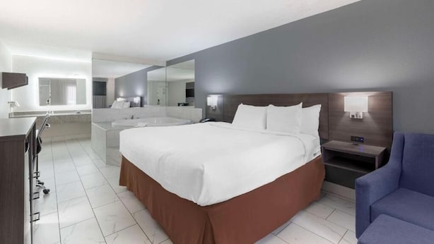 Een moderne hotelkamer met een groot bed, een nachtkastje, een stoel, een bureau en een badkamer met een spiegel en wastafel.