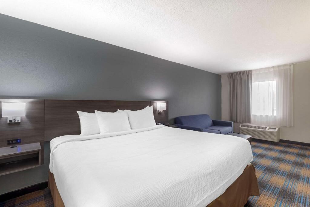 A hotel room with a large bed, a desk with a computer, a chair, and a window with curtains.