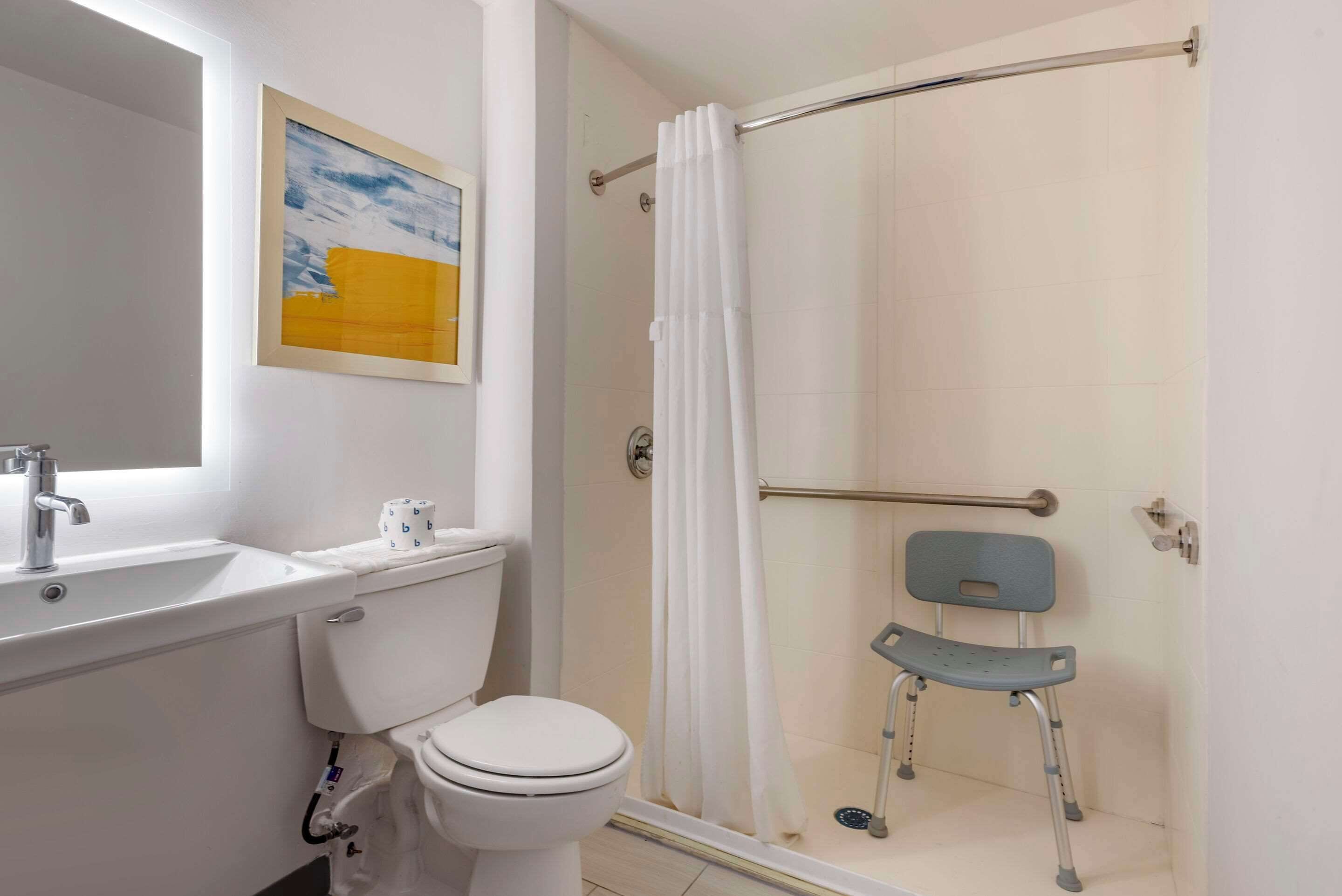 A bathroom with a toilet, sink, shower with a grab bar, and a wheelchair.
