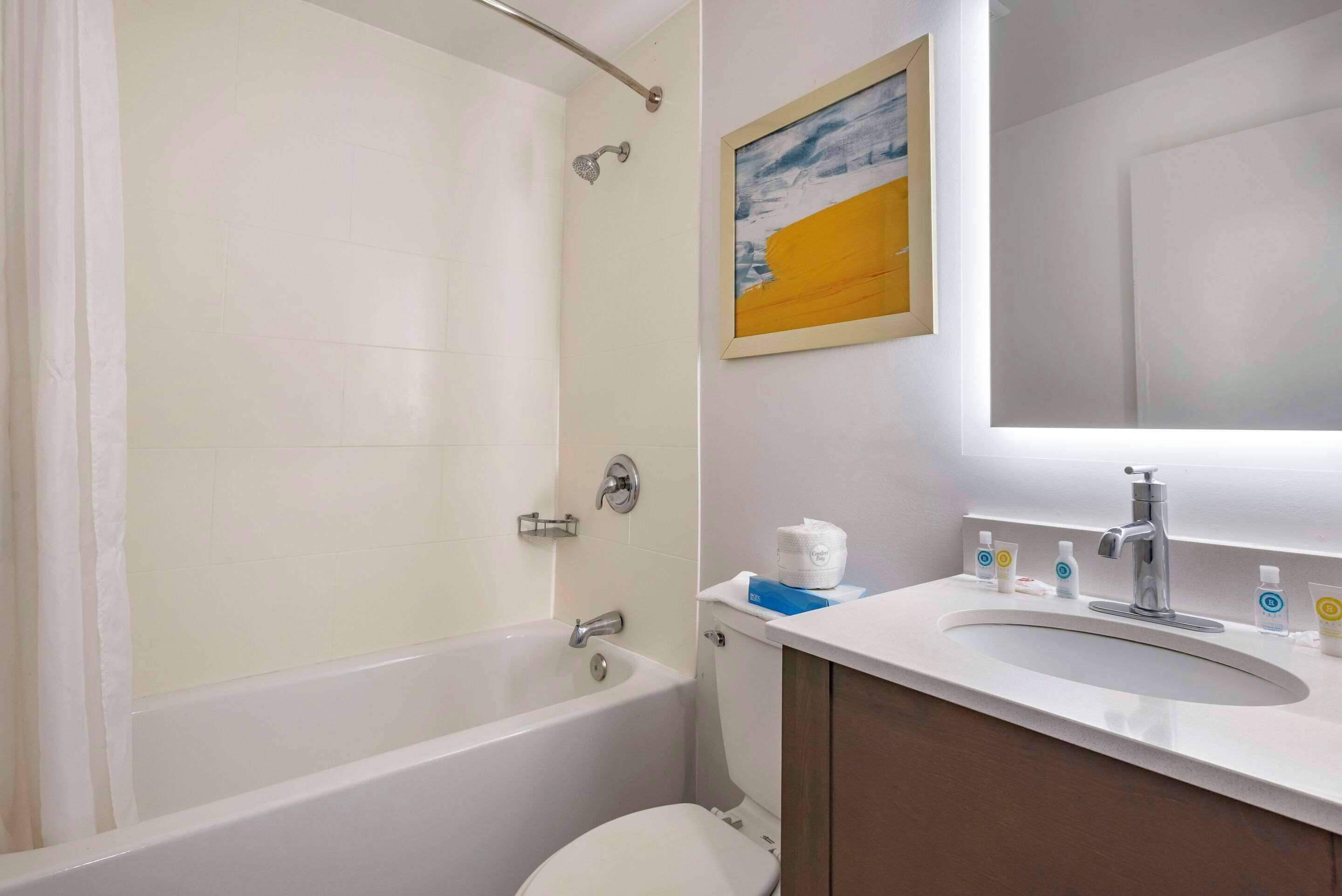 A bathroom with a bathtub, toilet, sink, and a framed painting on the wall.