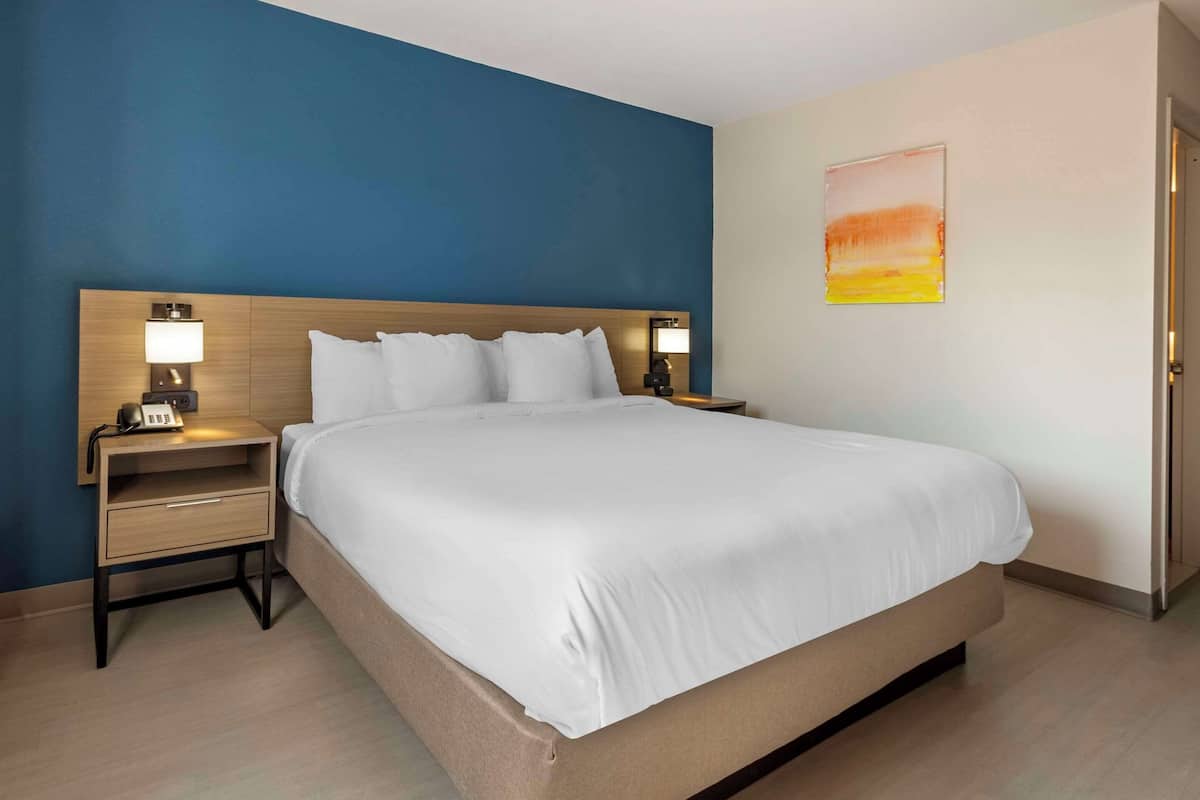 A hotel room with a large bed, two bedside tables with lamps, a nightstand with a phone, and a painting on the wall.