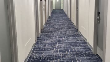 A long, narrow hotel hallway with a patterned carpet, white walls, and doors numbered 5 and 6.