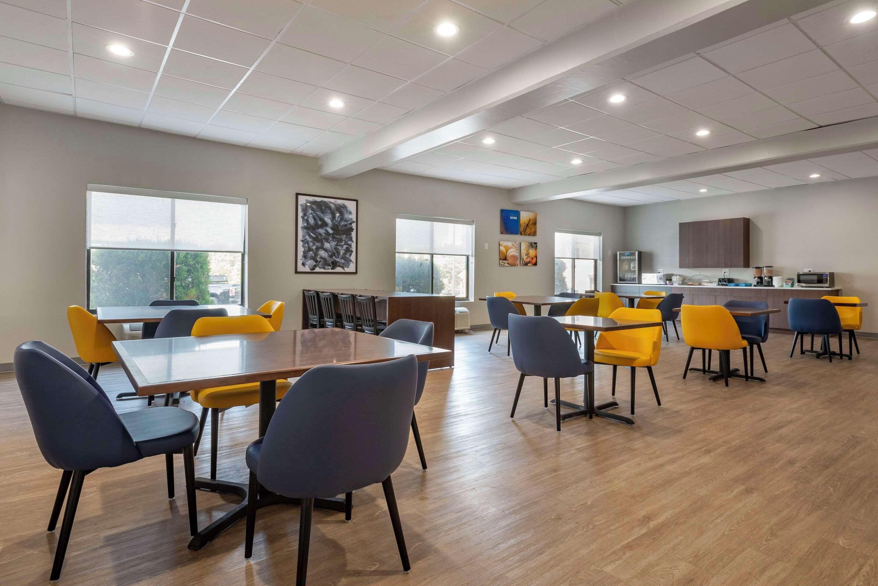 Un comedor amplio con varias mesas y sillas, ventanas grandes y una zona de cocina al fondo.