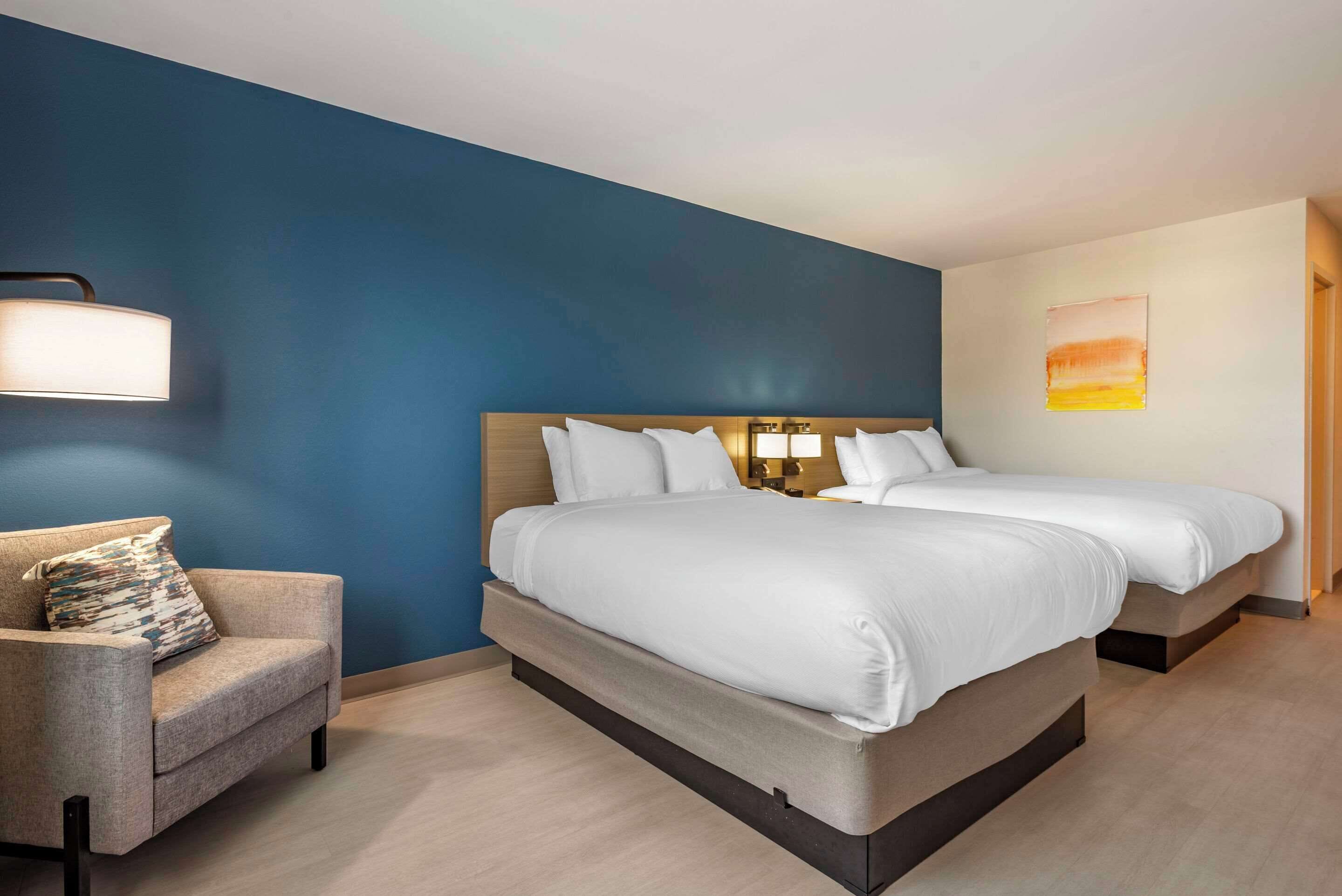A hotel room with a large bed, a chair, and a wall with a blue accent and a painting.