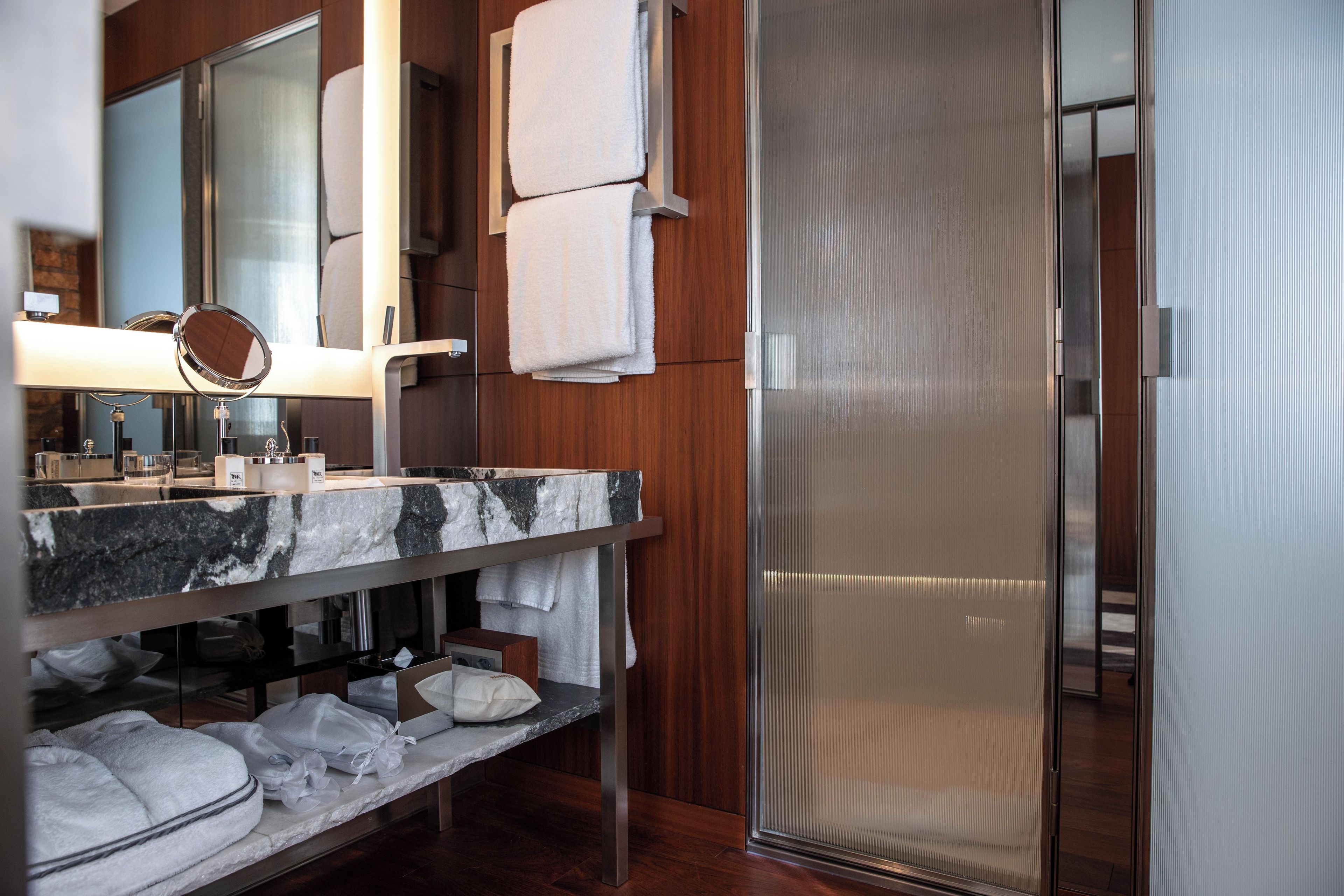 A modern bathroom with a marble sink, a mirror, and a glass shower enclosure.