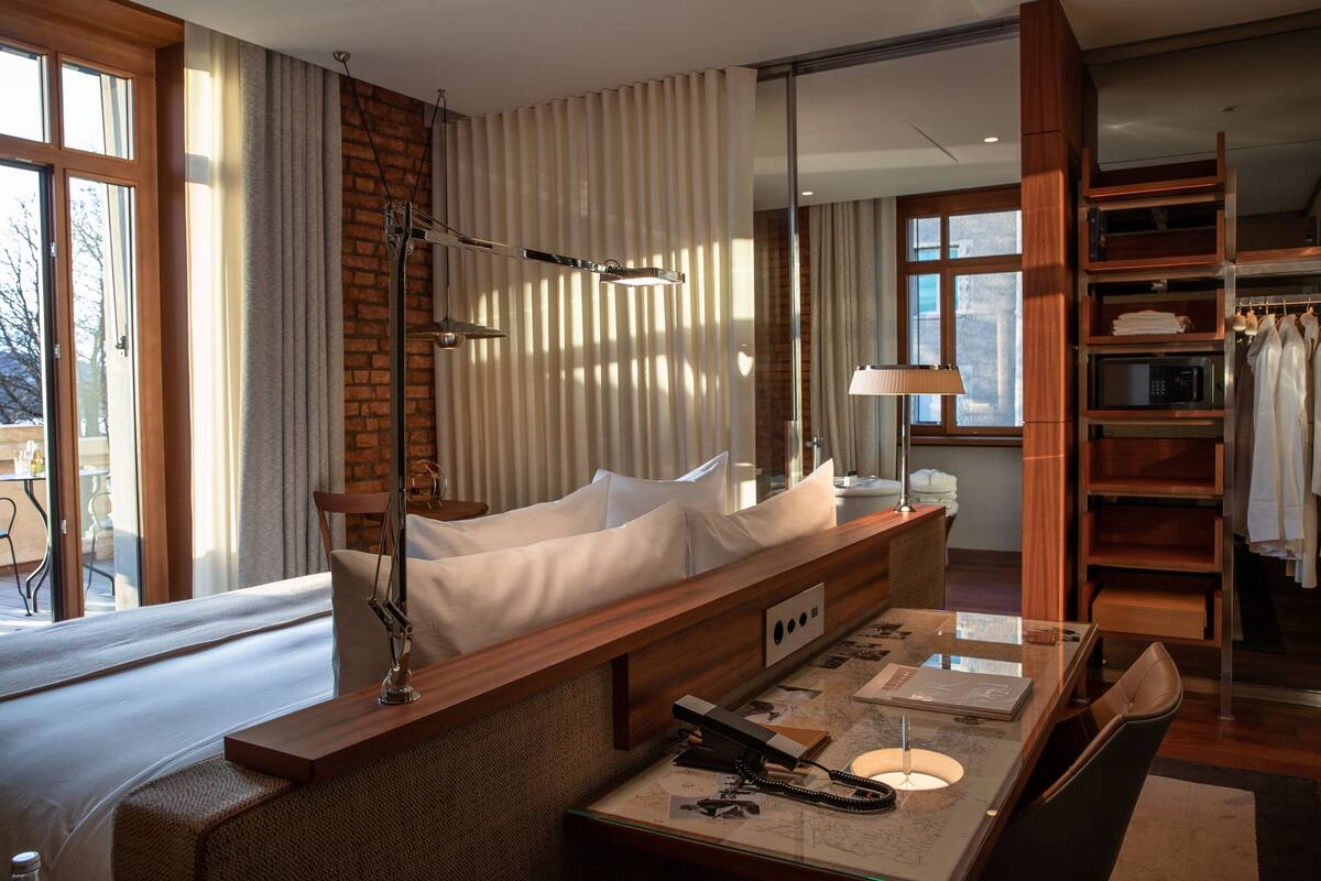 Een hotelkamer met een bed, een bureau met lamp, een spiegel, een kledingkast en uitzicht op het groen.