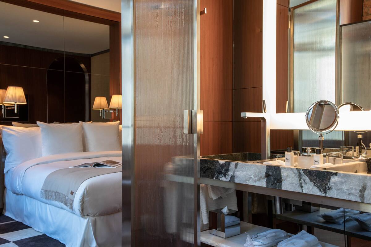 Een hotelkamer met een groot bed, een marmeren wastafel in de badkamer en een grote spiegel.