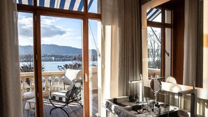 A balcony with a view of a lake and mountains, a seating area with a chair and table, and a bathroom with a sink and mirror.