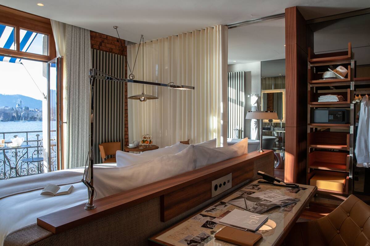 Een moderne hotelkamer met een groot bed, een houten nachtkastje, een bureau met stoel en uitzicht op zee.