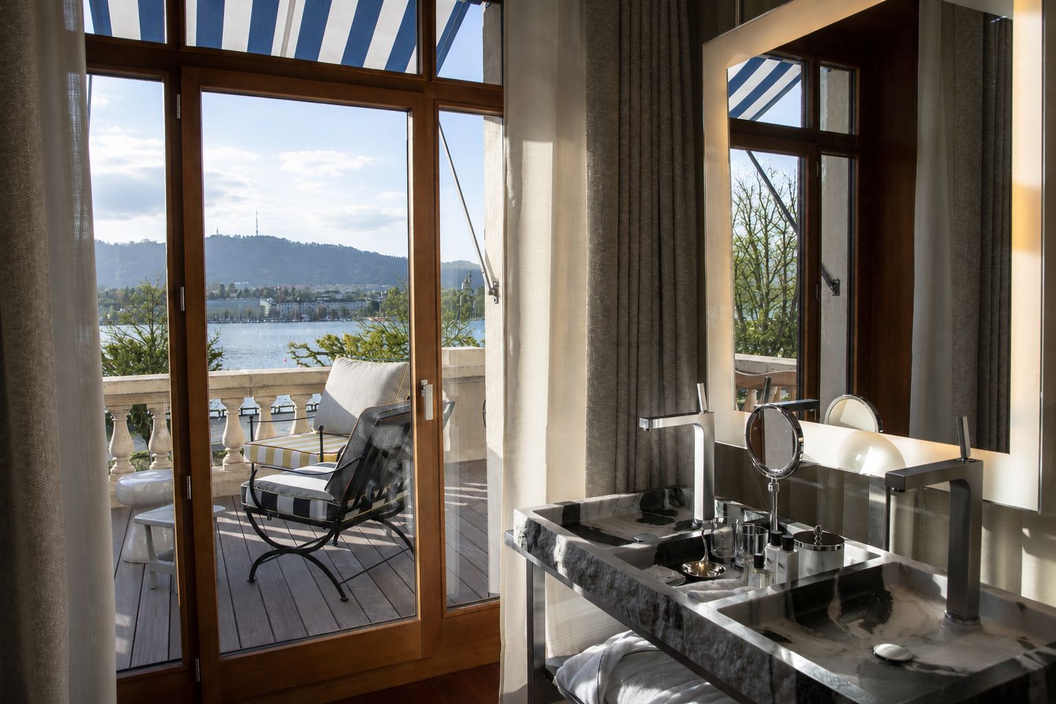 A bathroom with a large window, a sink, and a chair on a balcony.