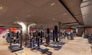 Une salle de sport équipée de divers appareils d’exercice, notamment des tapis de course, des appareils de musculation et un grand pilier central.