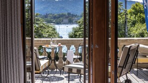 A terrace with outdoor seating, a view of a lake, and a mountainous backdrop.