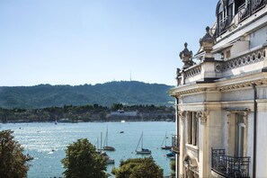 A coastal view with boats on the water, a building with ornate balconies, and a hill in the background. - La Réserve Eden au Lac Zurich (Zürich)