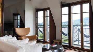A modern living room with a sofa, a chair, a small table with a book, and large windows with a view of a balcony and landscape.