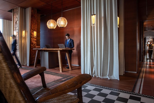 A modern hotel lobby with a wooden reception desk, a checkered floor, and a man working on a laptop.