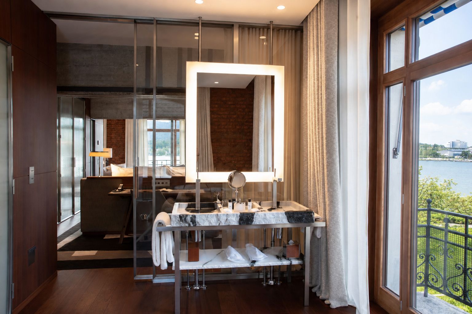 A modern bathroom with a marble sink, a large mirror, and a view of a body of water through the window.