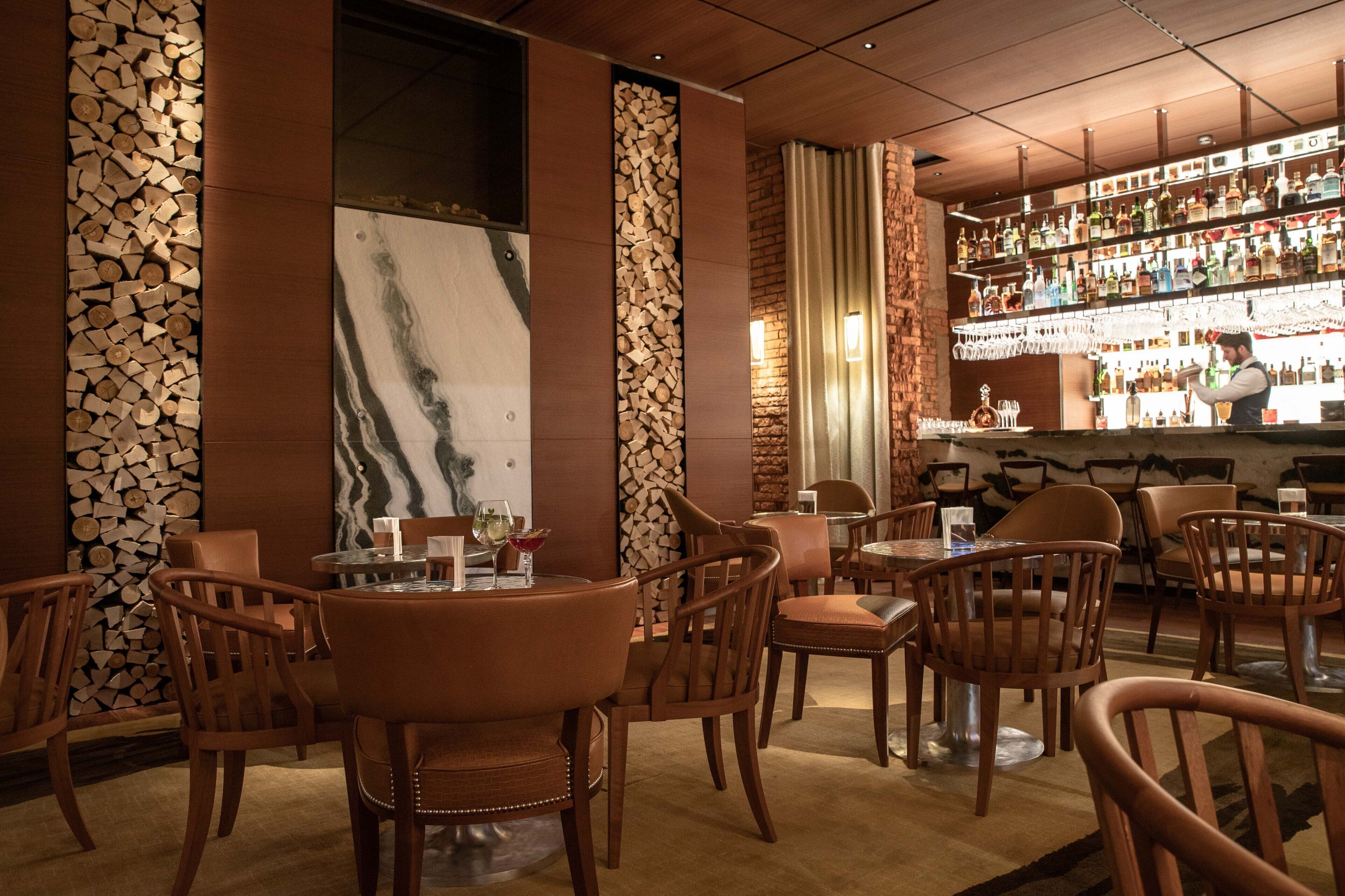 A bar area with wooden chairs and tables, a bar counter with bottles, and a large marble wall.