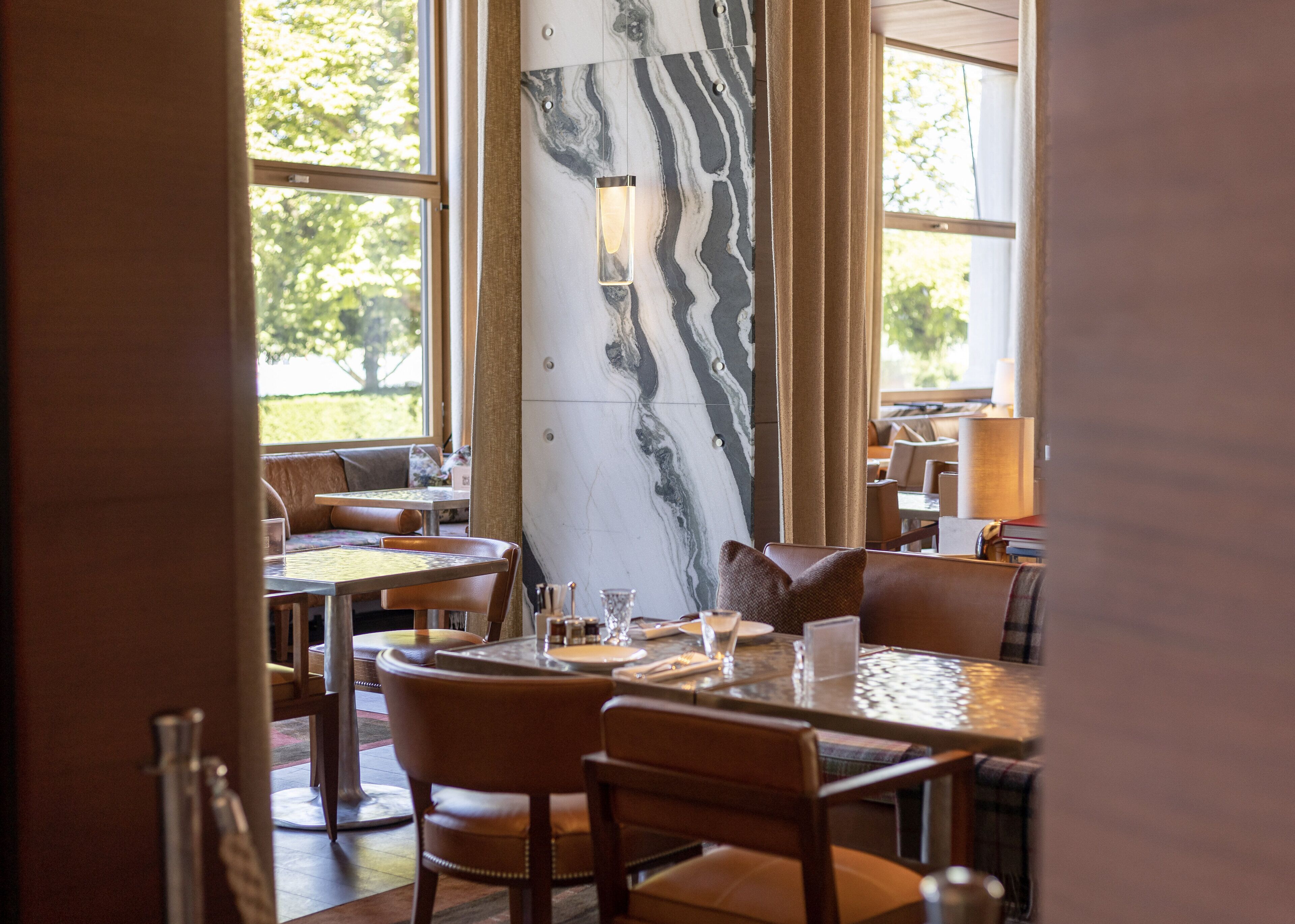 Ein Restaurant mit Marmorwänden, Ledersitzmöbeln und Blick auf Grünflächen.