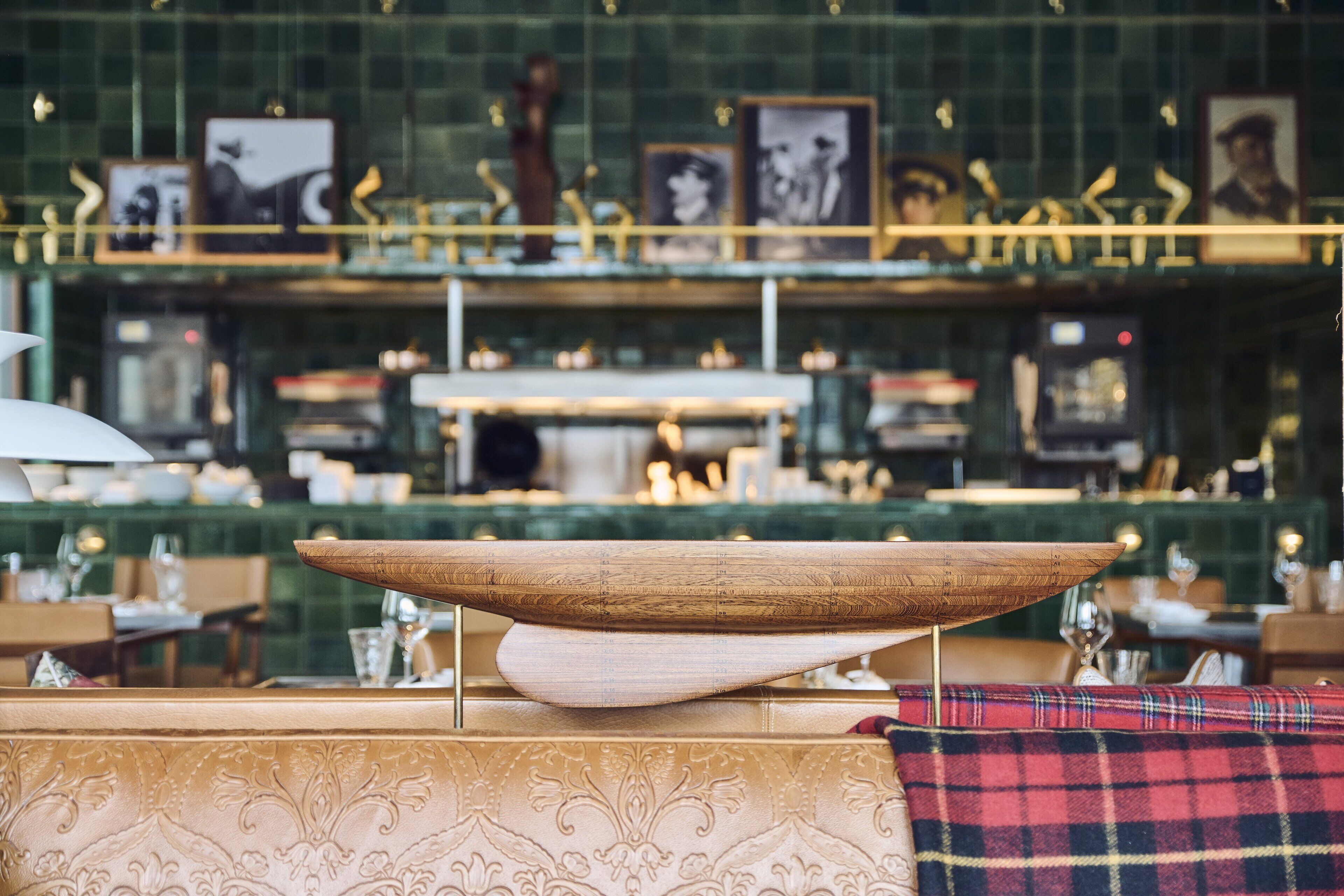 Zona de bar con un cuenco de madera como centro, pared de azulejos verdes y cuadros enmarcados.