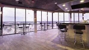 A spacious bar area with high ceilings, large windows offering views of the surrounding landscape, and modern bar stools.