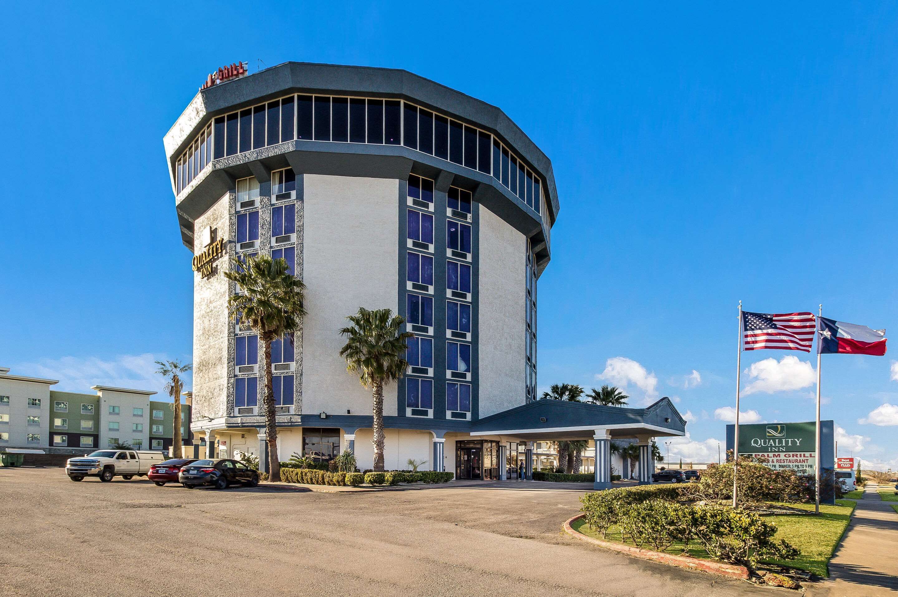 A hotel with a curved corner design, a palm tree, and a sign indicating a Quality Inn.
