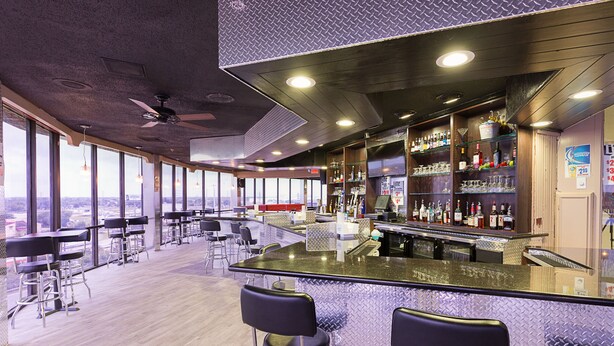 A modern bar area with a glass counter, bar stools, and a variety of bottles.