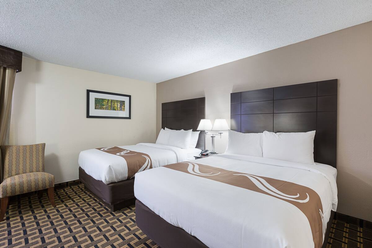 A hotel room with two beds, a chair, a framed picture on the wall, and a patterned floor.