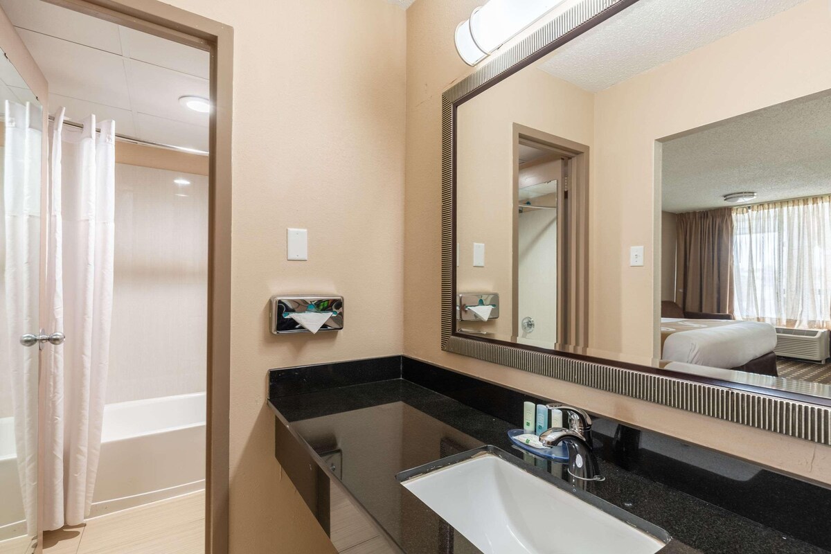 A hotel bathroom with a bathtub, a sink, a mirror, and a shower area.